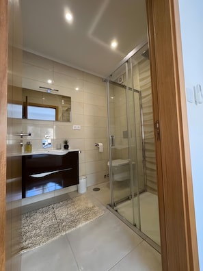 Uma casa de banho moderna com cabine de duche em vidro, toucador com espelho e sanita.