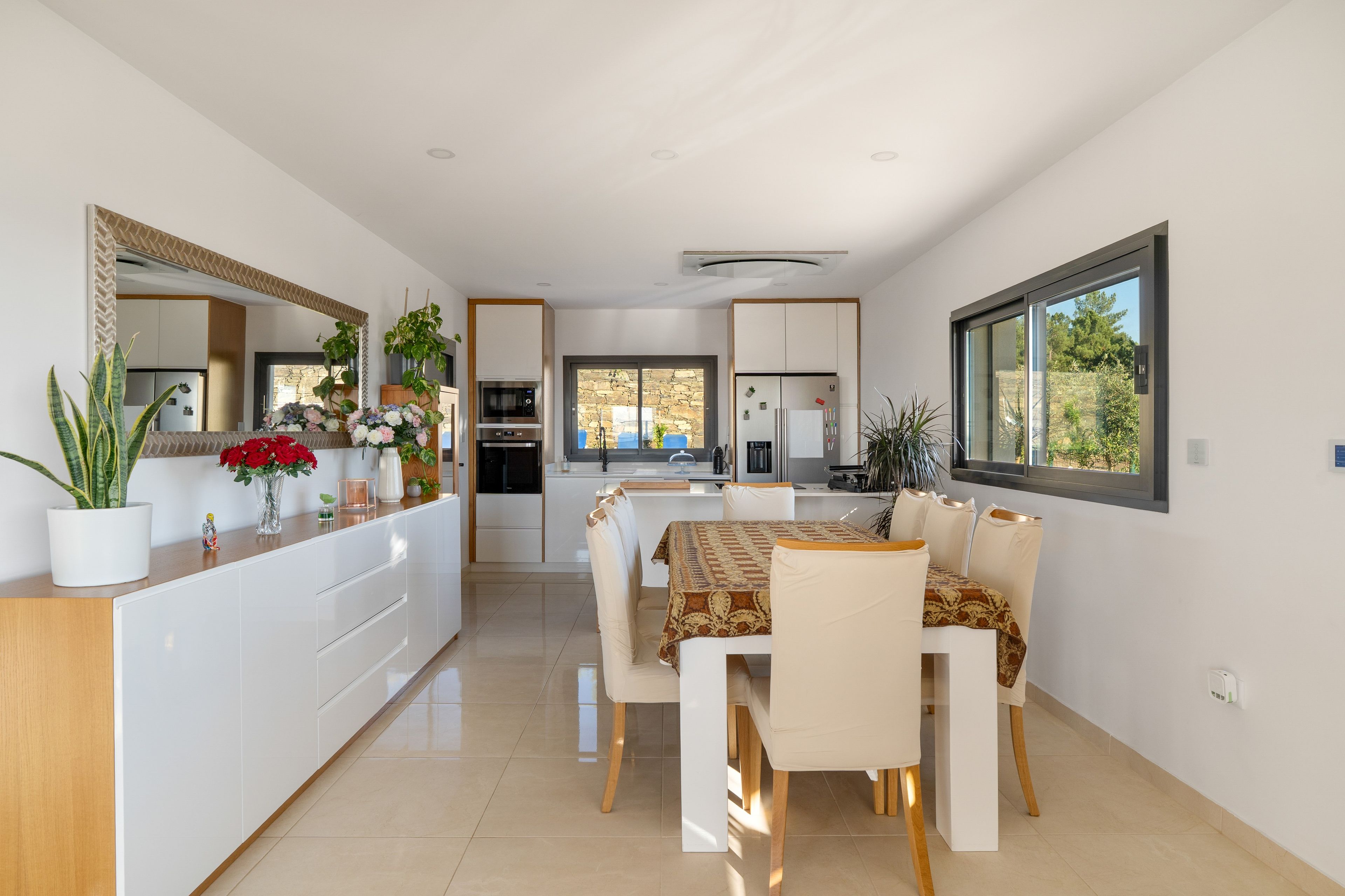 Una cocina y comedor moderna con armarios blancos, una isla central con plantas y una mesa de comedor lista para cuatro.