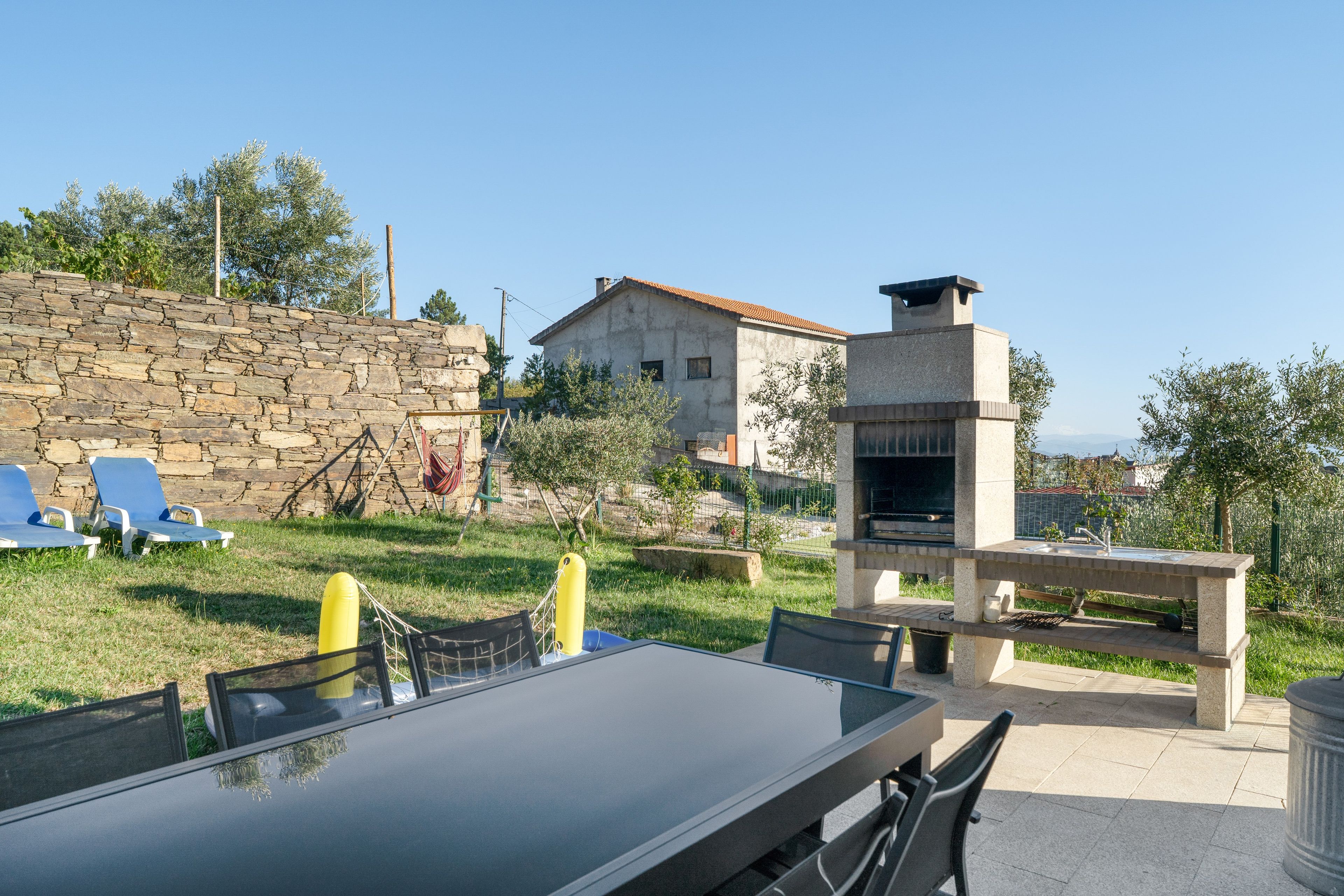 A patio with a table and chairs, a stone wall, and a house in the background.