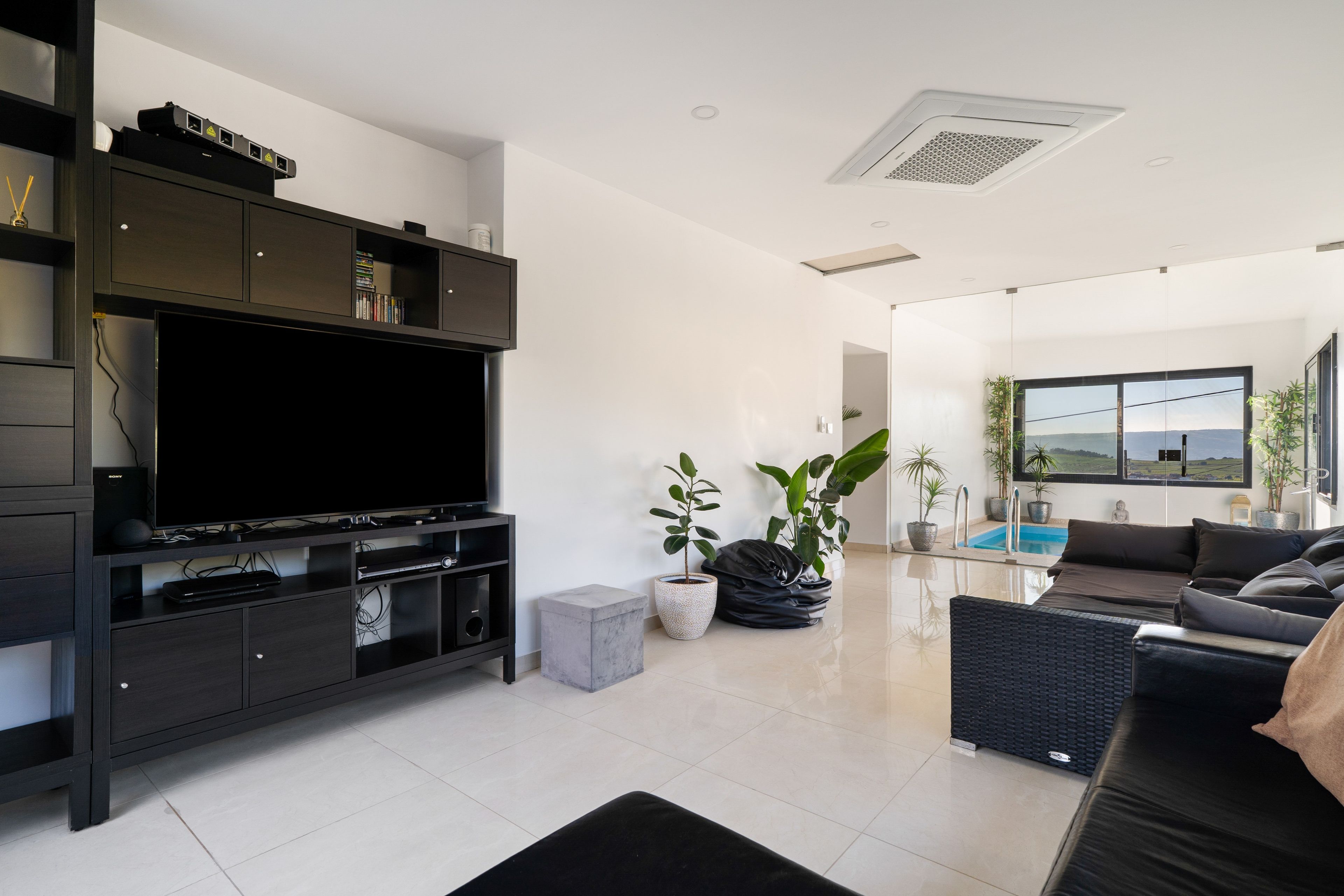 Una sala de estar moderna con televisor de pantalla plana, muebles oscuros, una pequeña piscina y vistas al exterior.