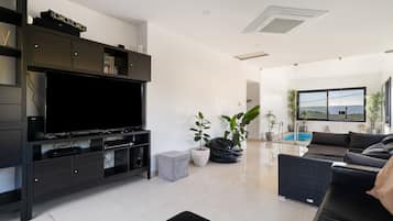 Una sala de estar moderna con televisor de pantalla plana, muebles oscuros, una pequeña piscina y vistas al exterior.