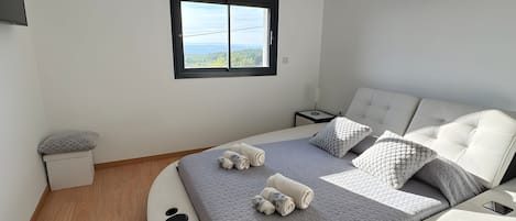 Une chambre à coucher moderne avec un lit aux lignes courbes, une vue par la fenêtre et une table de chevet.