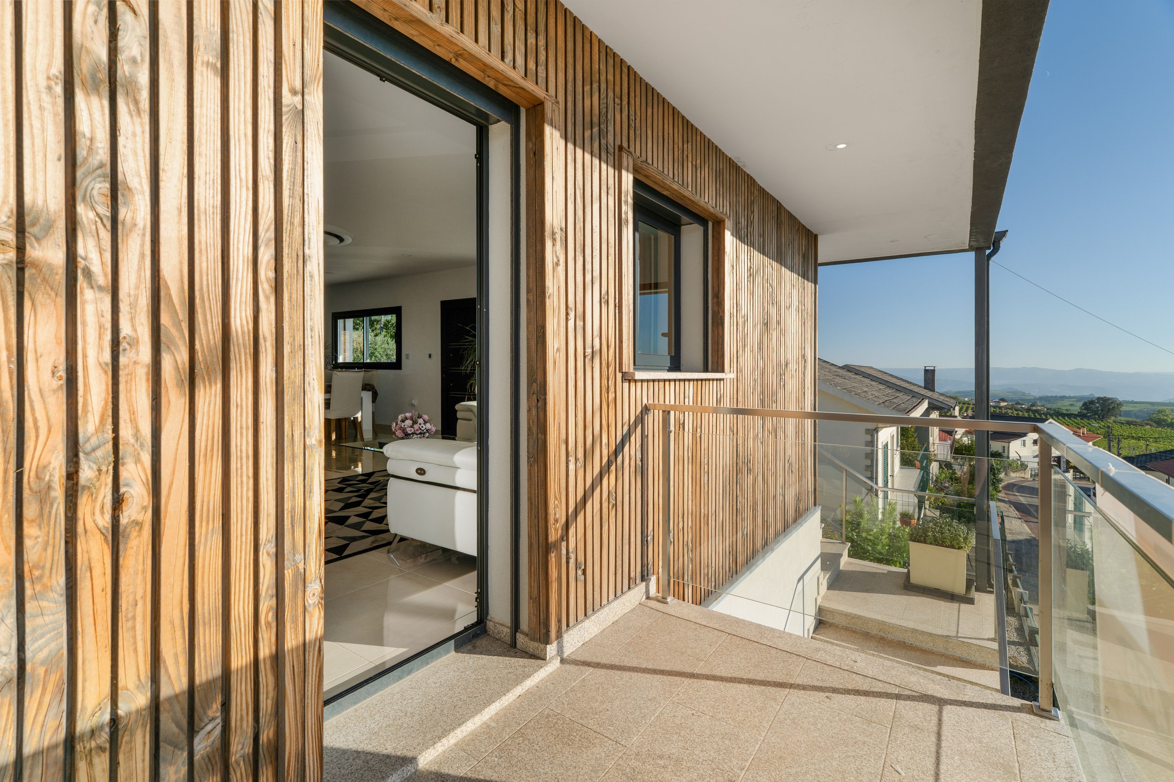 Un interior moderno con revestimiento de madera, un balcón con barandilla de vidrio y vistas al campo.