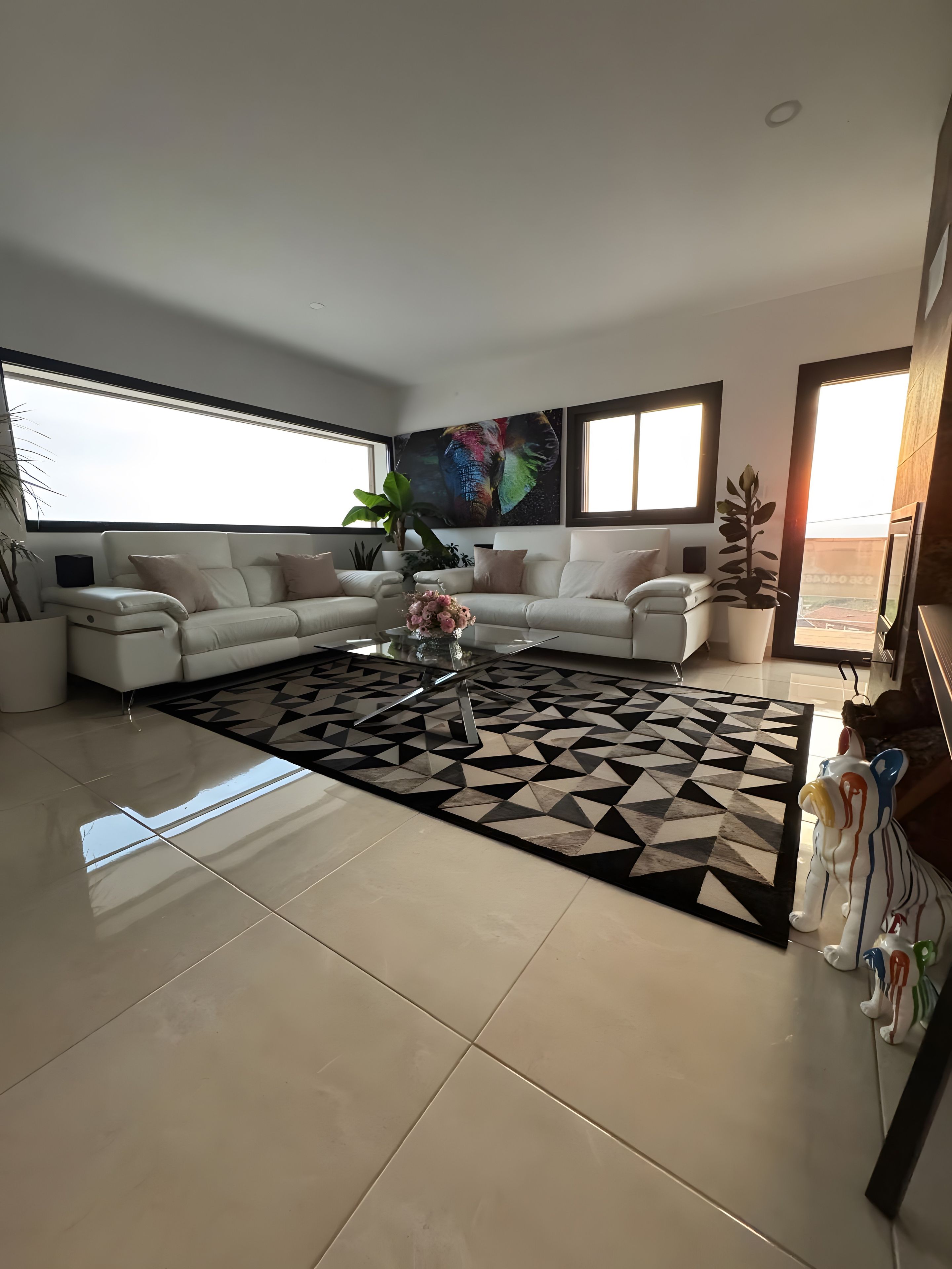 Una sala moderna con un sofá modular, una mesa de centro con flores y una alfombra geométrica.