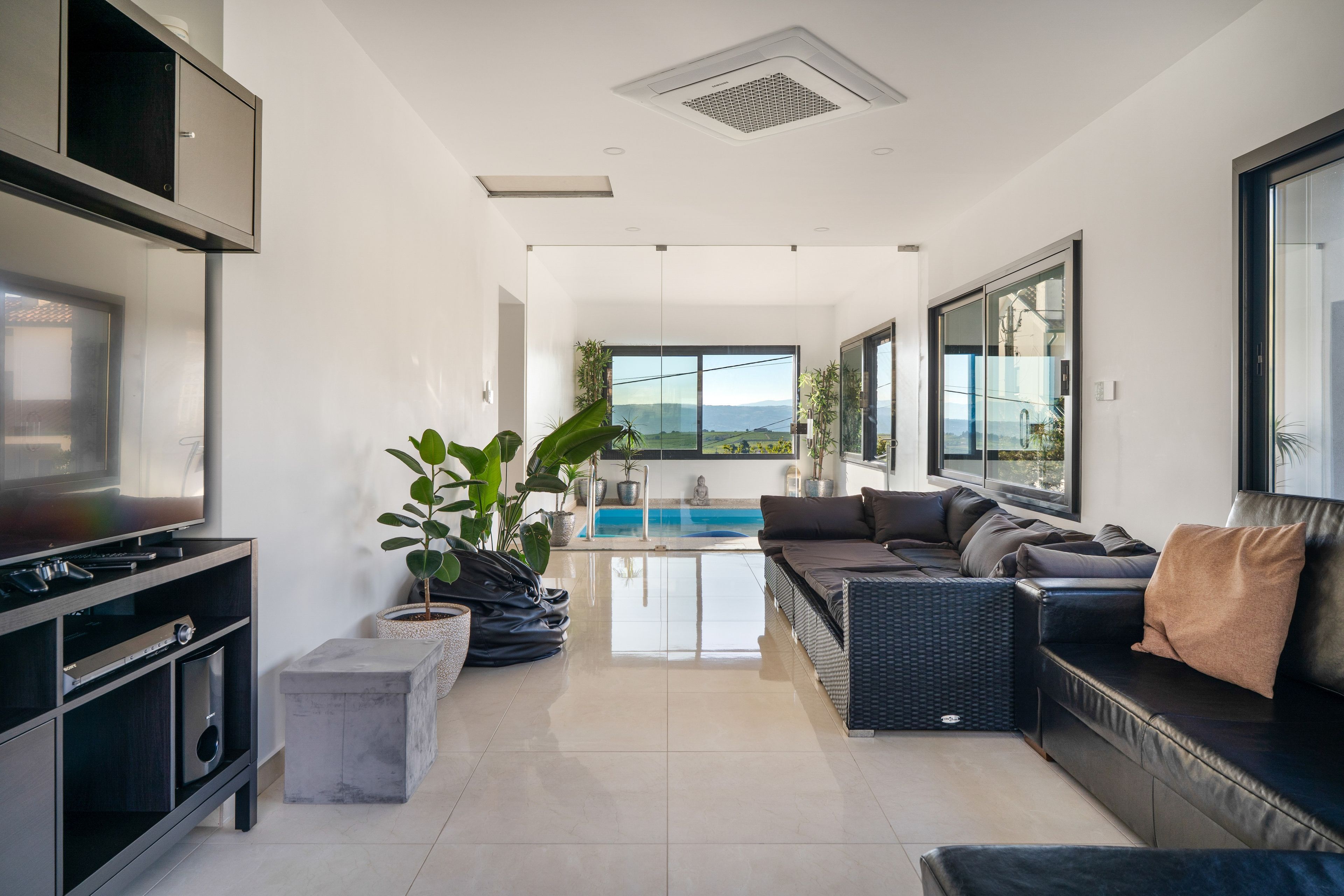 A modern living room with a flat-screen TV, comfortable seating, a pool, and a view of the outdoors.