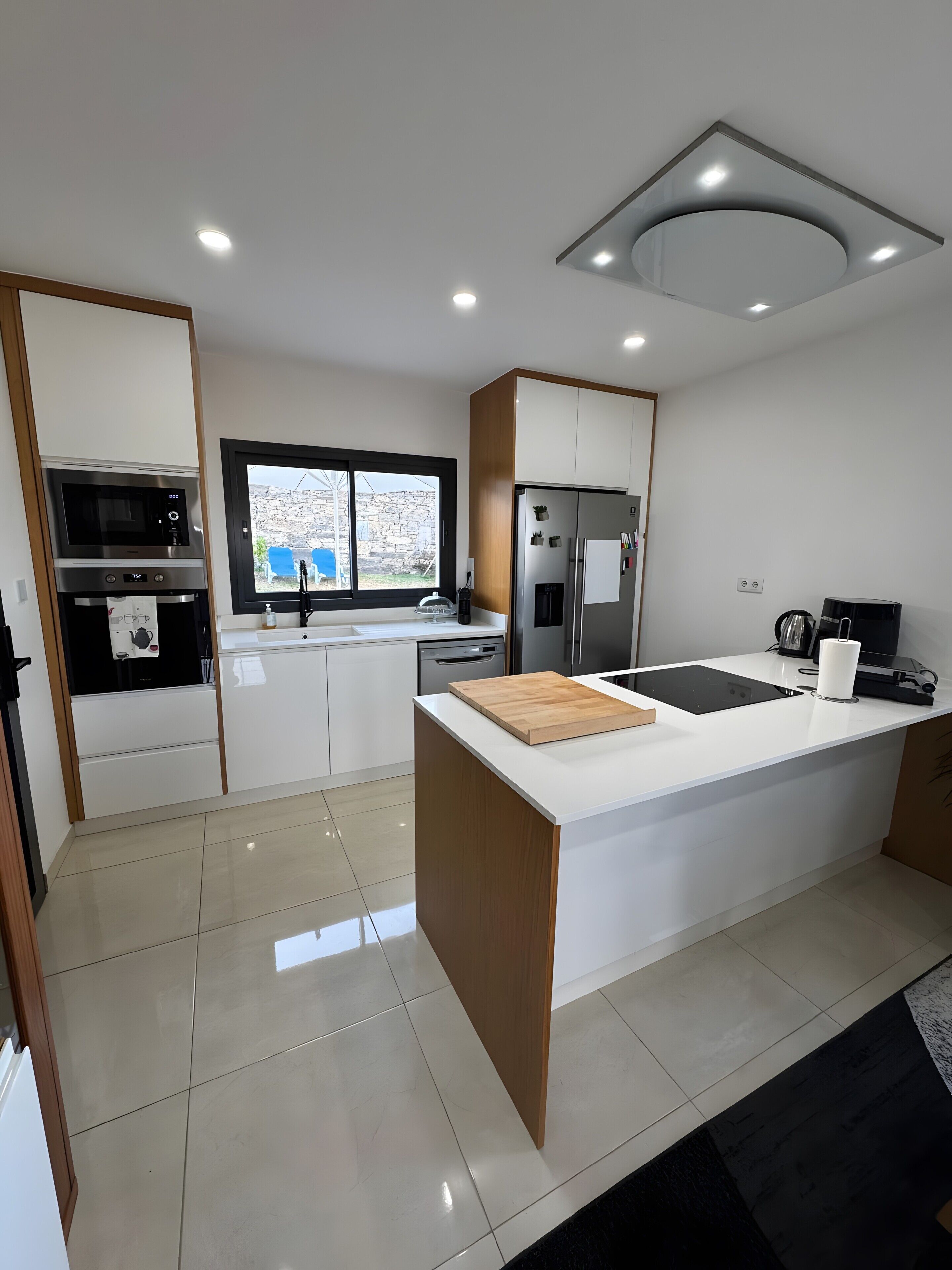 A modern kitchen with a central island, built-in appliances, and a view through a window.