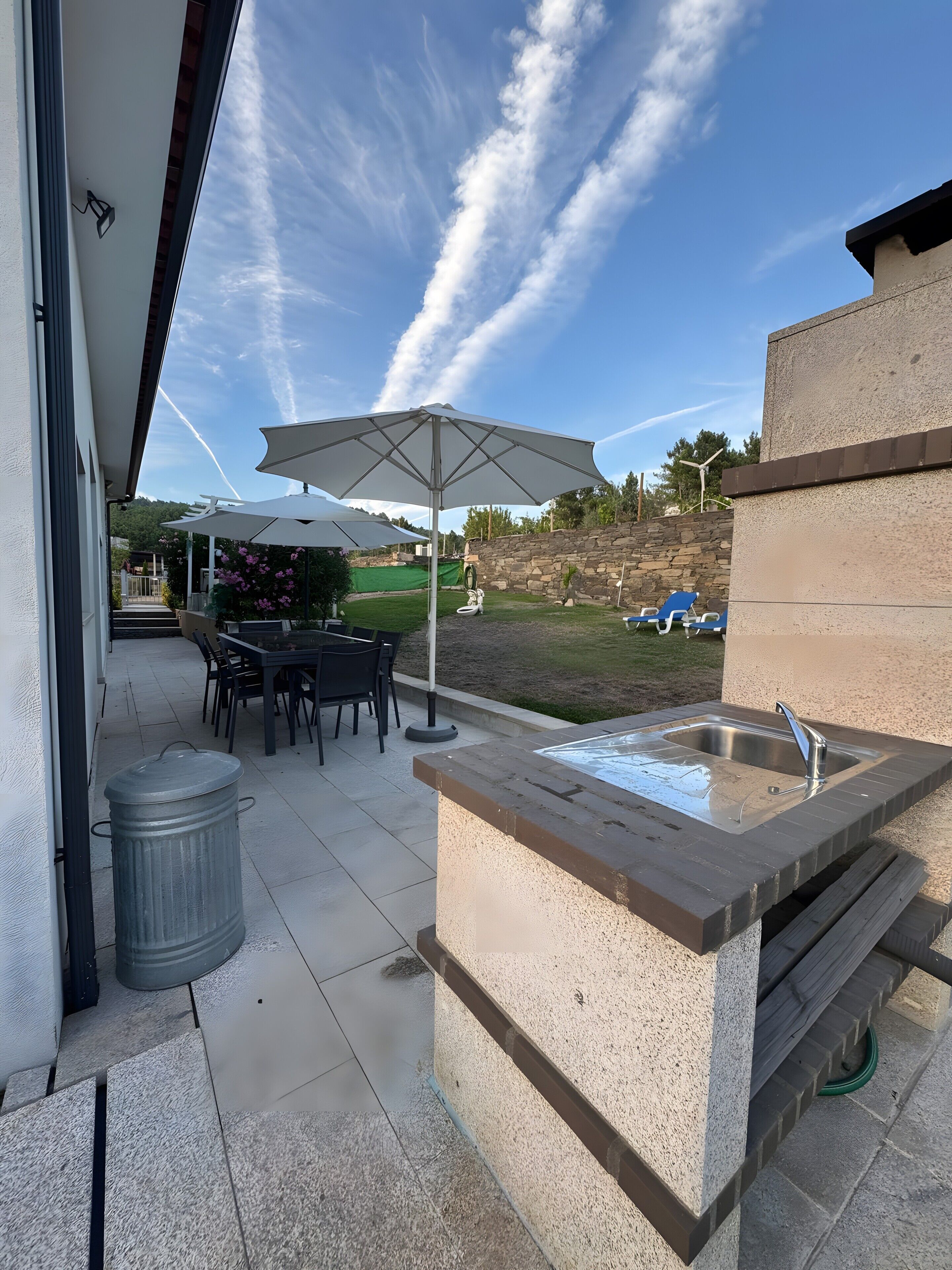 An outdoor patio with a stone sink, a table with chairs, and umbrellas.