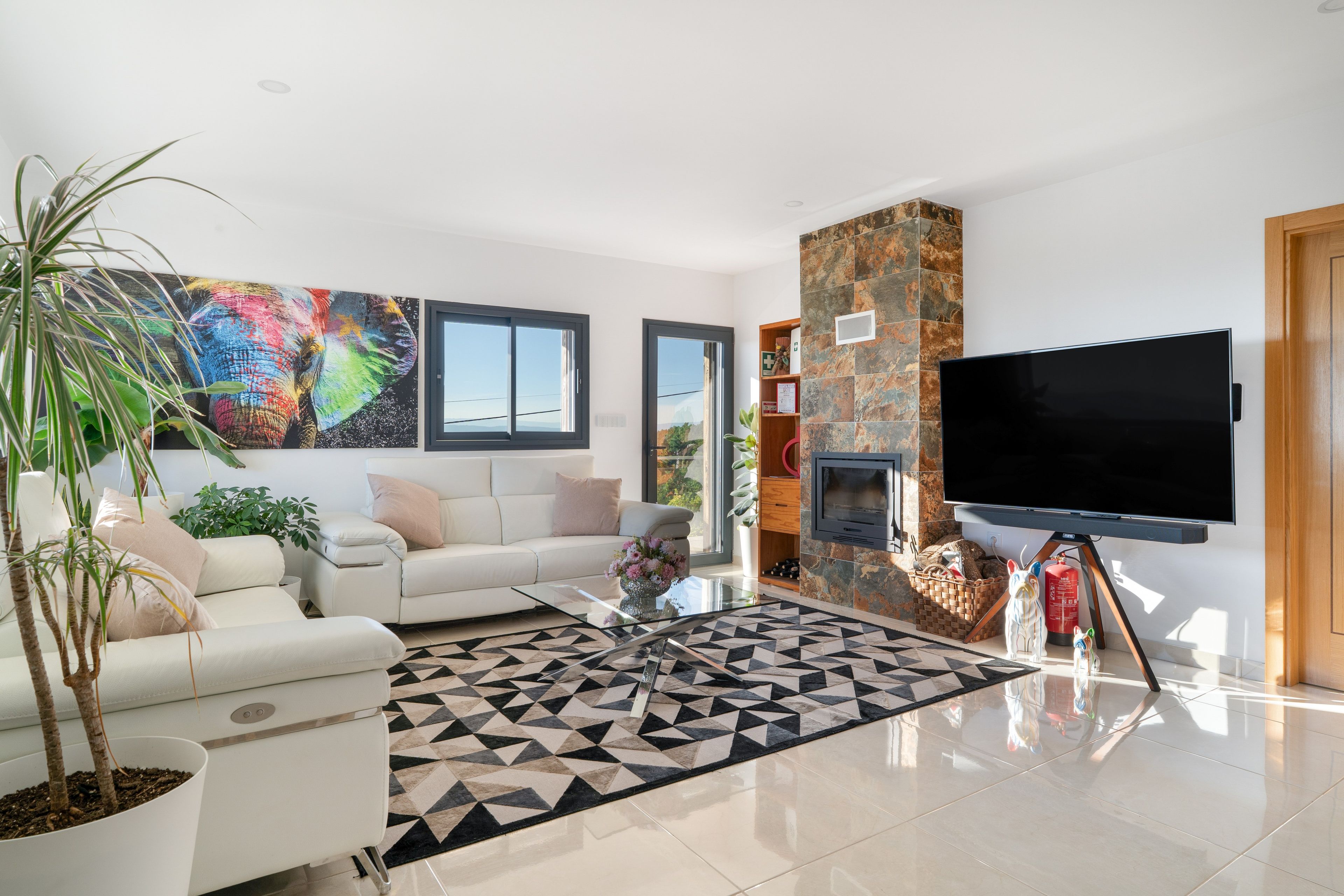 Una sala de estar moderna con un sofá blanco, un televisor de pantalla plana, chimenea y un ventanal grande.
