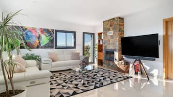 Una sala de estar moderna con un sofá blanco, un televisor de pantalla plana, chimenea y un ventanal grande.