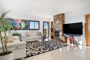 A modern living room with a white sofa, a flat-screen TV, a fireplace, and a large window.