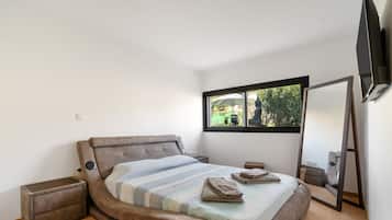 Un dormitorio moderno con una cama grande, una mesita de noche, un mueble auxiliar, una ventana con vistas a zonas verdes y un televisor de pared.