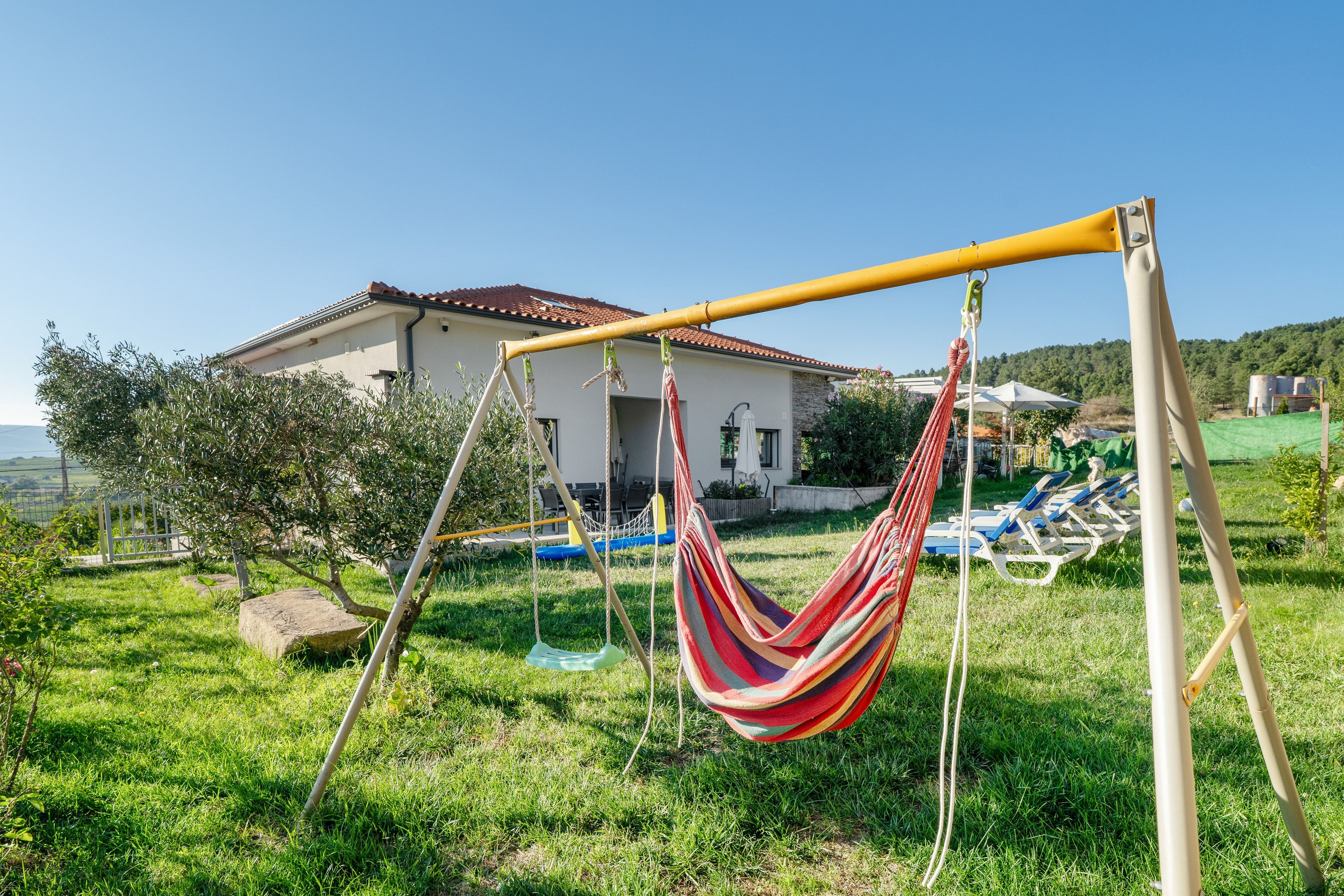 A hammock suspended over a grassy area with a house in the background.