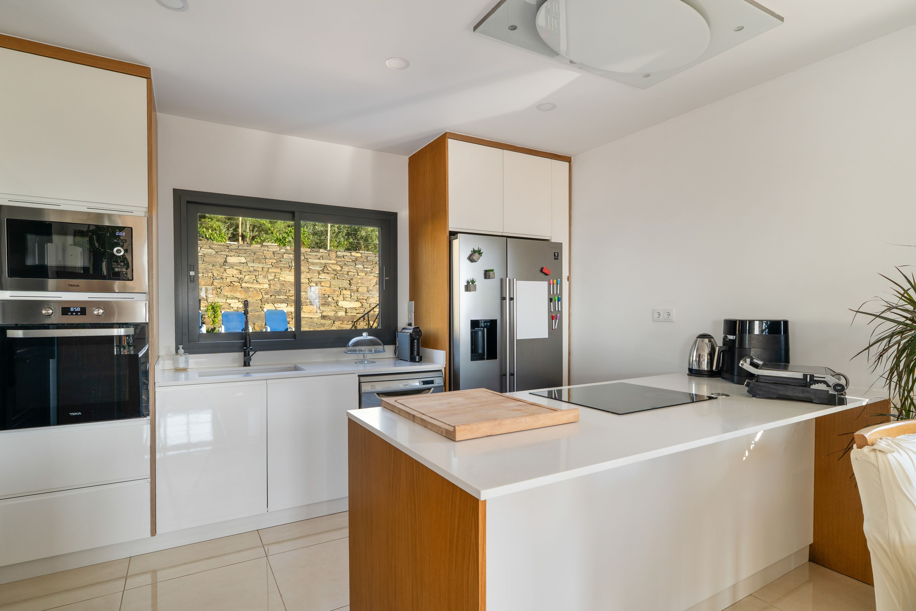 A modern kitchen with white cabinetry, a built-in oven, a refrigerator, and a coffee maker.