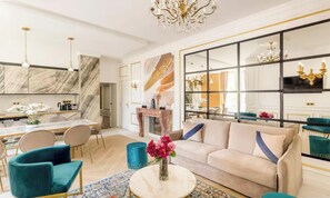 A modern living room with a sofa, chairs, a coffee table, and a dining area with a kitchen in the background. - A PEACEFUL & REFINED RETREAT IN THE HEART OF THE RIVE GAUCHE – RUE DU BAC (Paris)