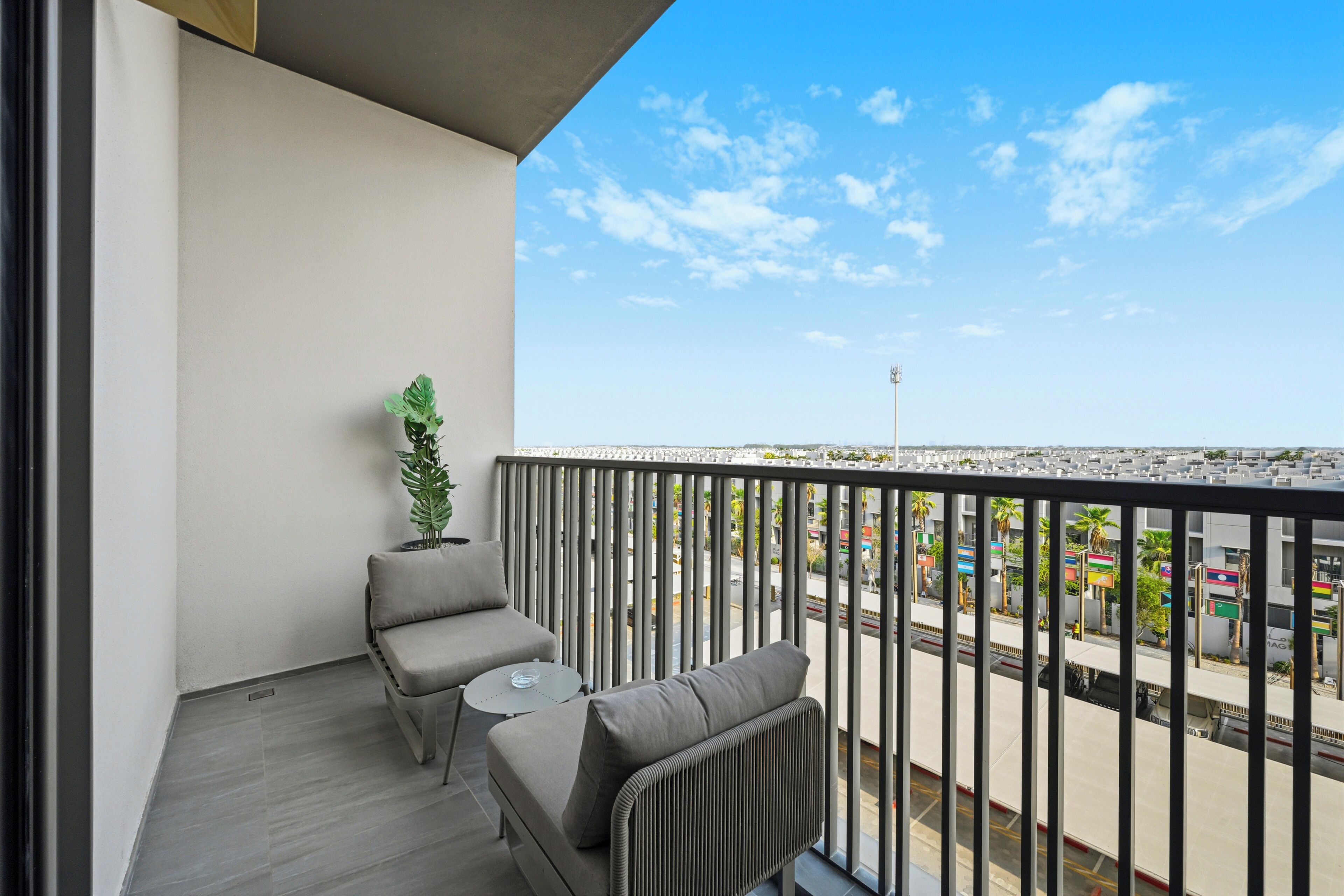 Een balkon met een grijze bank, een klein rond tafeltje en een plant in een pot.