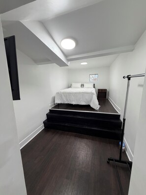 Een slaapkamer met een bed, een raam en een trap naar een hoger gelegen verdieping.