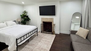 A modern bedroom with a bed, a sofa, a fireplace, and a TV mounted on the wall. - 2-bedroom Bronzeville Gem (Chicago)