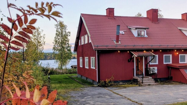 Une maison en bois rouge, avec un toit en pente, un porche à l’avant et un petit garage attenant.