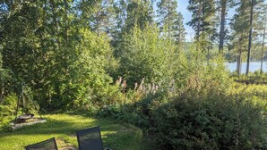 Une table en bois avec deux chaises, placée dans un espace verdoyant, entourée d’une végétation luxuriante, et offrant une vue sur un lac.