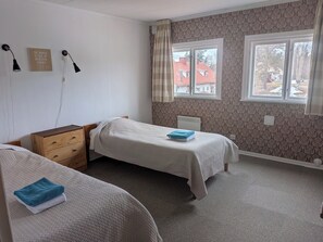 A bedroom with two single beds, a wooden dresser, a radiator, and a window with a view of buildings outside. - Spacious homes with river views (Ytterhogdal)