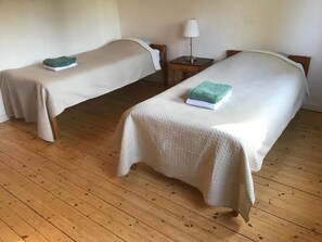 Two single beds with white bedding, a wooden floor, and a bedside table with a lamp.