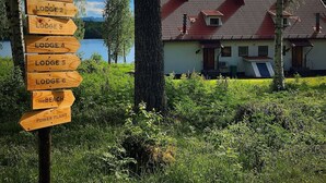 Un panneau indicateur en bois, indiquant les directions vers différents chalets et une plage, avec une maison et des arbres en arrière-plan.