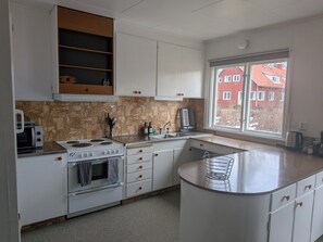 Una cocina con armarios blancos, estufa, microondas y ventana con vista a edificios.