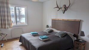 Une chambre à coucher comprenant un lit, deux lampes de chevet, un radiateur, une fenêtre avec des rideaux et une décoration murale représentant un crâne de cerf.