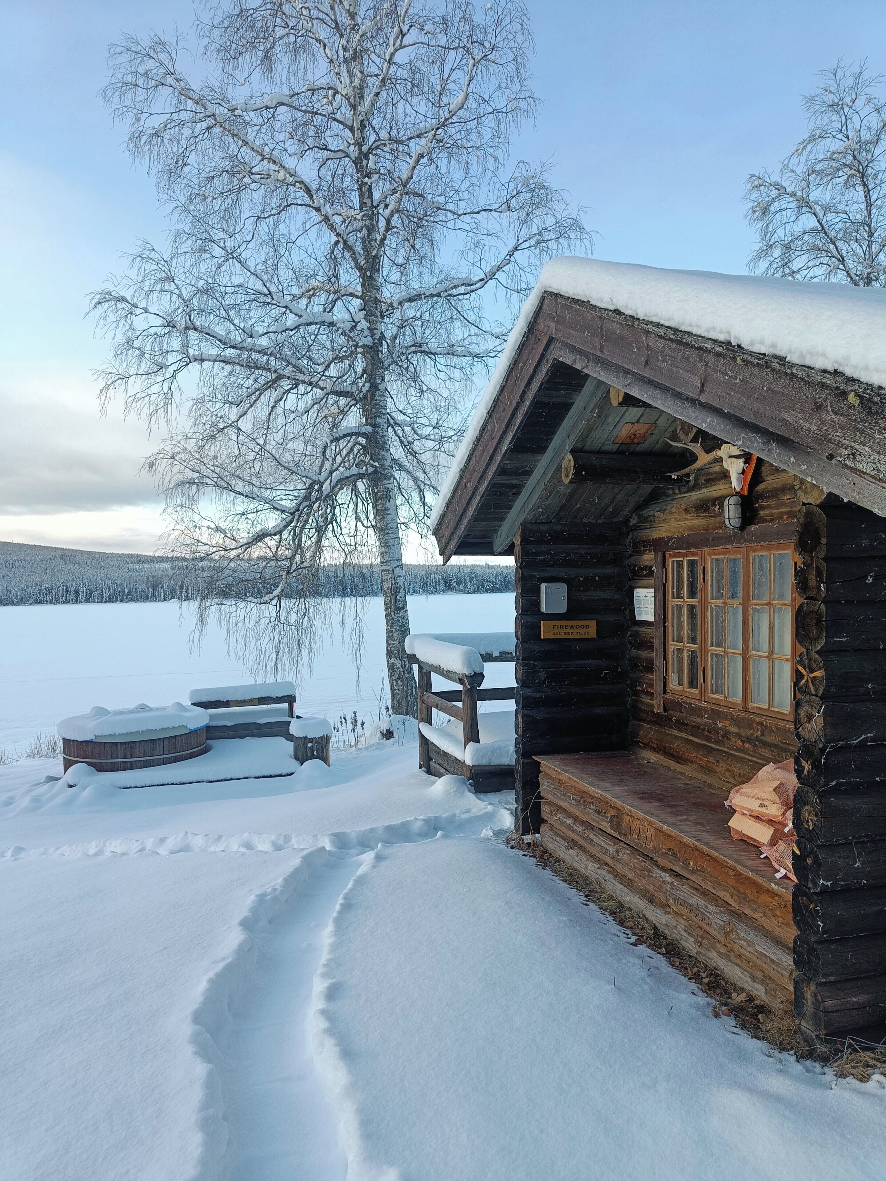 En hytte med træterrasse og et snødekt landskap.