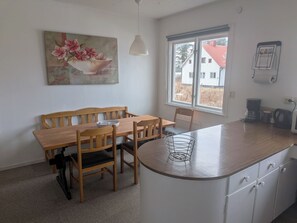 A dining area with a wooden table and chairs, a white cabinet with drawers, a window with a view of buildings, and a painting on the wall. - Vrbo Property (Ytterhogdal)