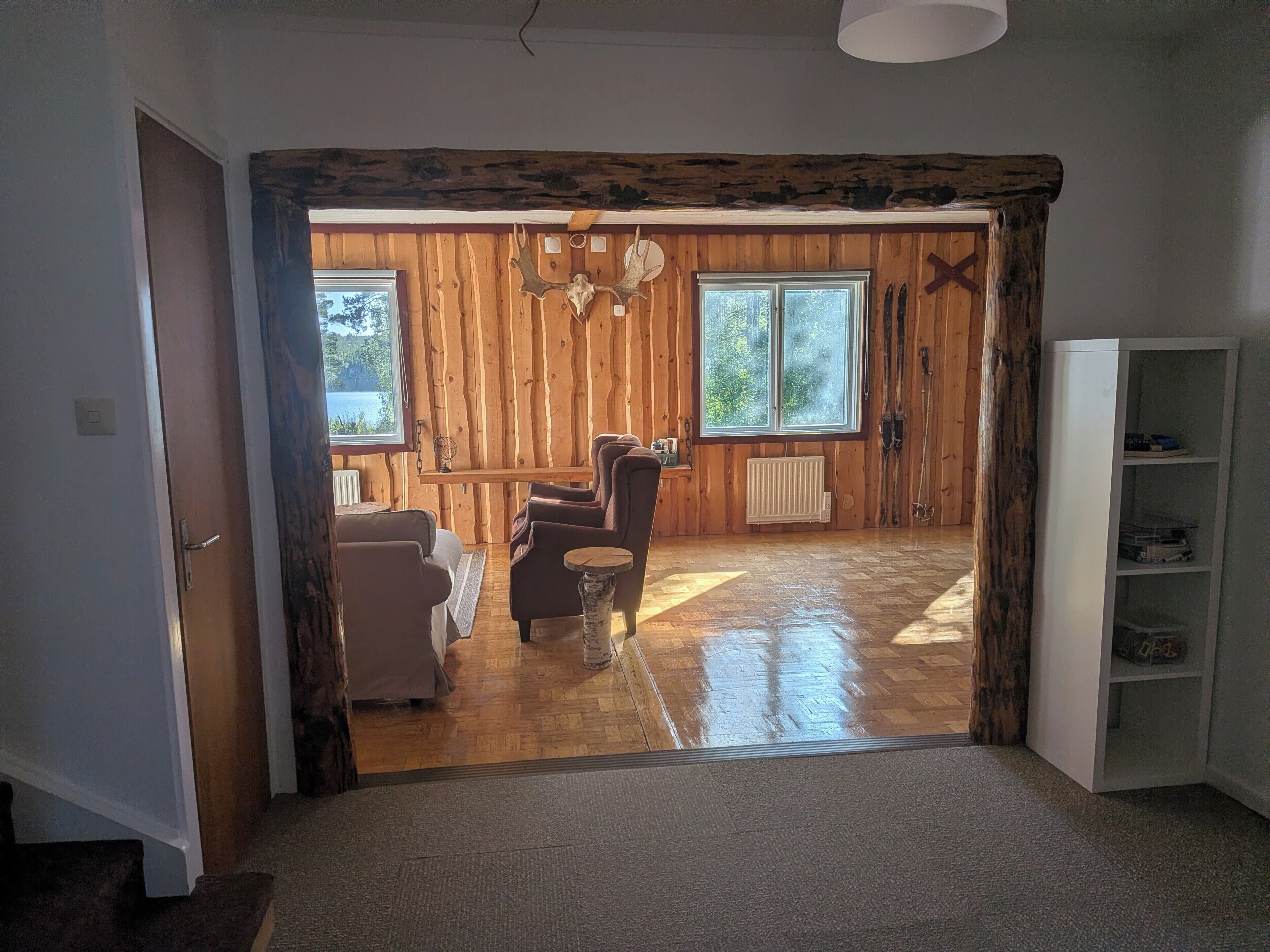 Un interior de madera con un sofá, sillas, un radiador y una ventana con vistas a follaje.