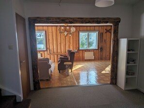 A wooden interior with a sofa, chairs, a radiator, and a window overlooking greenery. - Spacious homes with river views (Ytterhogdal)