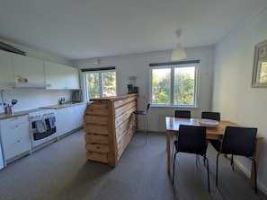 A compact kitchen with a wooden island, a dining area with a table and chairs, and a window providing a view of trees.