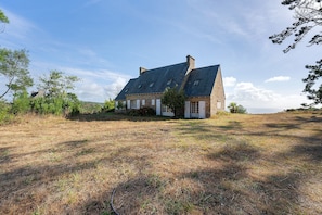 A stone house with a sloped roof, surrounded by a grassy field and trees.