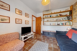 A living room with a television, a sofa, a bookshelf, and framed fish illustrations on the wall.
