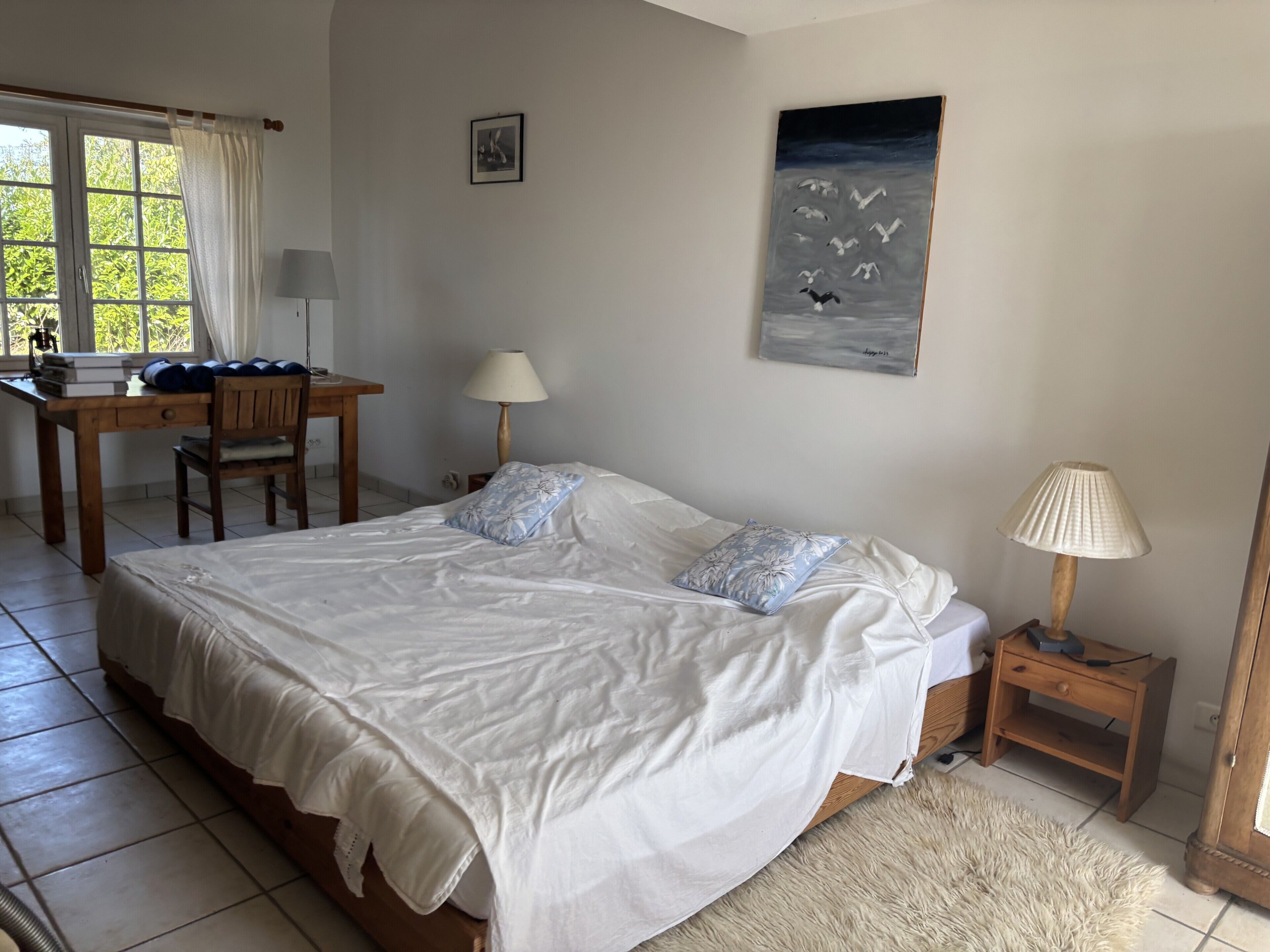 Un dormitorio con una cama grande, un escritorio, una silla, una lámpara y un cuadro en la pared.
