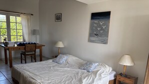 Ein Schlafzimmer mit einem großen Bett, einem Schreibtisch, einem Sessel, einer Lampe und einem Gemälde an der Wand.