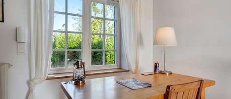 A wooden table with a lamp, a window with curtains, and a radiator.