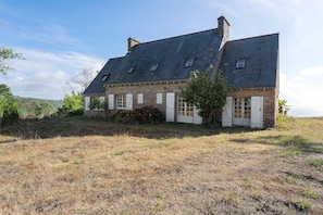 Ein Steinhaus mit einem steilen Satteldach, zahlreichen Fenstern und einem gepflegten Rasen.