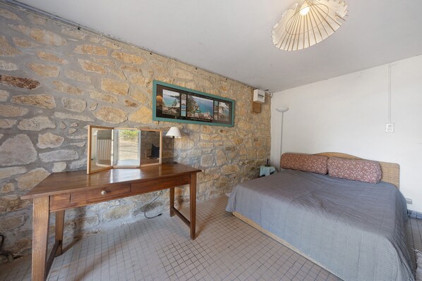 Un dormitorio con pared de piedra, un escritorio de madera, una cama con ropa de cama estampada y un cuadro en la pared.