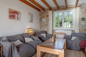 Ein gemütliches Wohnzimmer mit Steinwand, Holzbalken, einem großen Fenster und einem Kamin.