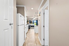 Un corridoio con porte bianche, una zona cucina con frigorifero e un'area pranzo con tavolo e sedie.