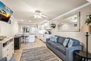 A modern kitchen with white cabinets, a microwave, and a stove. There is a gray sofa with blue cushions and a small table beside it. - 🐾 Sunset Harbor Palms 2-102 | Pet Friendly Studio on Santa Rosa Sound (Navarre Beach)