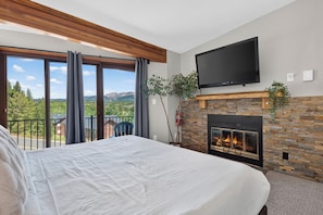 Ein Schlafzimmer mit einem großen Bett, einem Kamin, einem Fernseher und einem Balkon mit Bergblick.