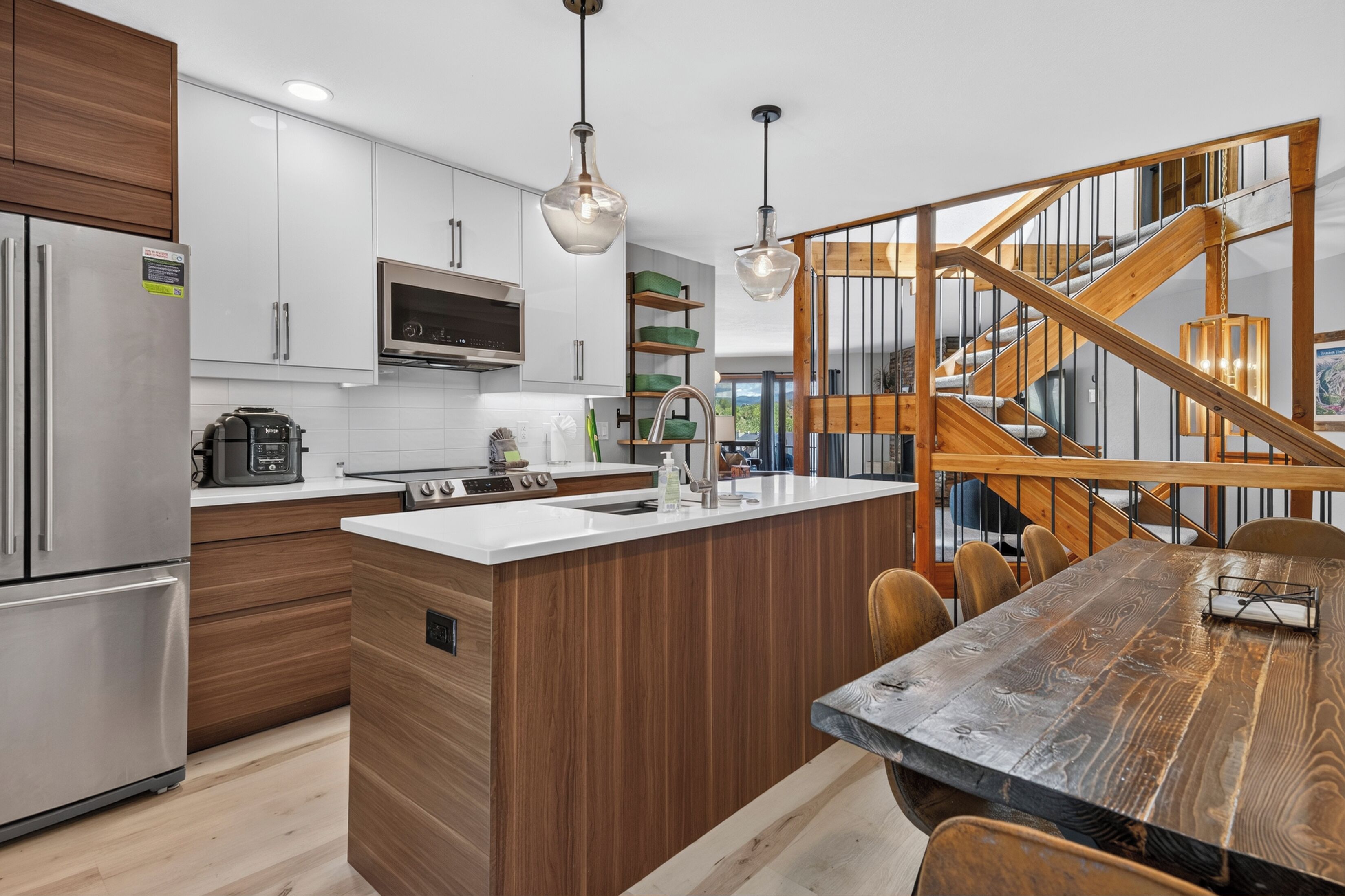 A modern kitchen with a central island, stainless steel appliances, and a wooden staircase.
