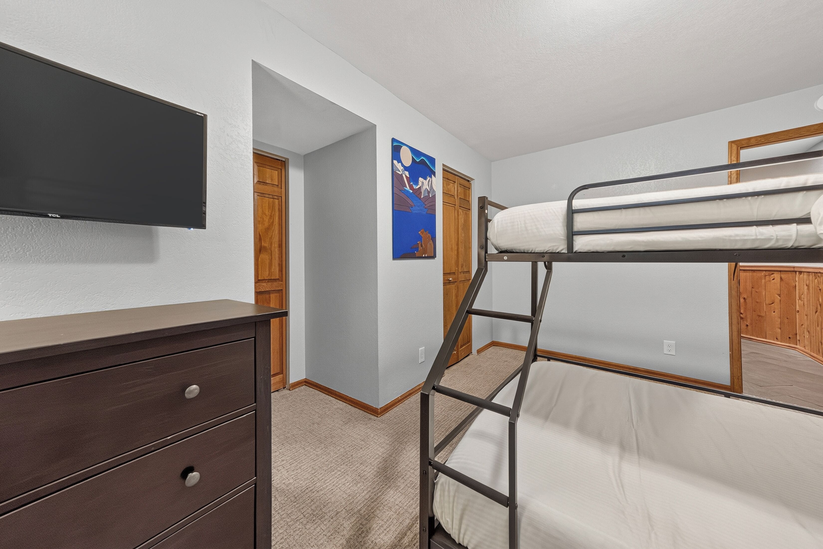 A room with a bunk bed, a dresser, a television, and a door leading to another room.