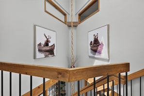Eine Treppe mit hölzernen Geländern und einer weißen Wand, die zwei Bilder von Elchen in Booten zeigt.