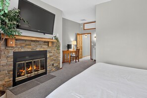 A modern bedroom with a fireplace, a flat-screen TV mounted above it, a desk with a chair, and a large bed. - Walk to Downtown townhome. Private Hot Tub. Views. Sleeps 12 (Winter Park)