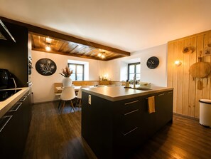 Una cuina moderna amb una illa central, sostre de fusta i zona de menjador amb cadires.