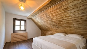 Un dormitorio con techo inclinado, una ventana, un banco de madera y una cama con ropa blanca.
